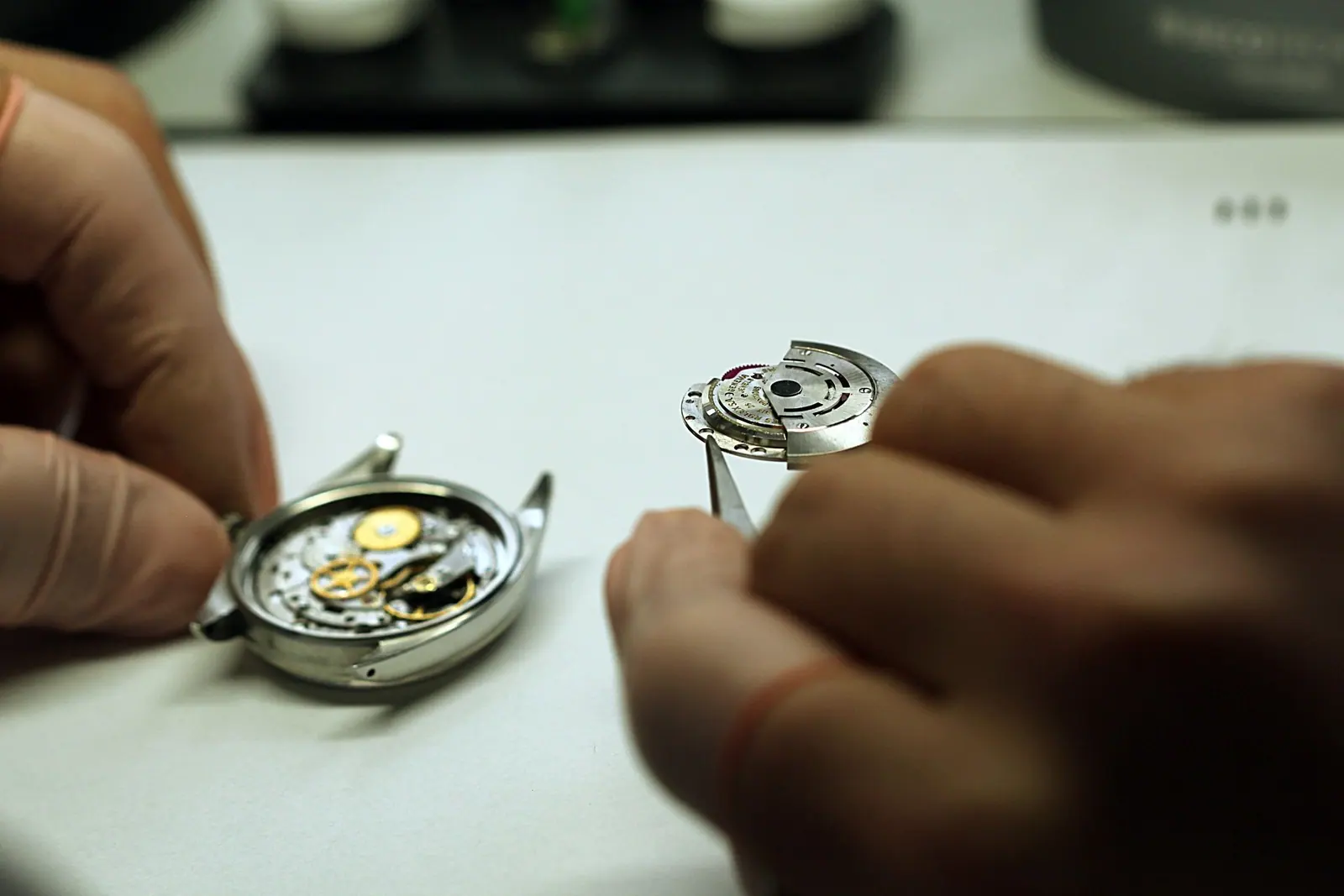 Manos de un relojero trabajando en un reloj con unas pinzas.